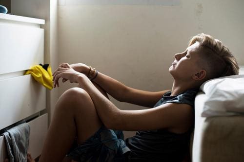 a boy who could benefit from teen suicide prevention programs sits on a floor looking depressed